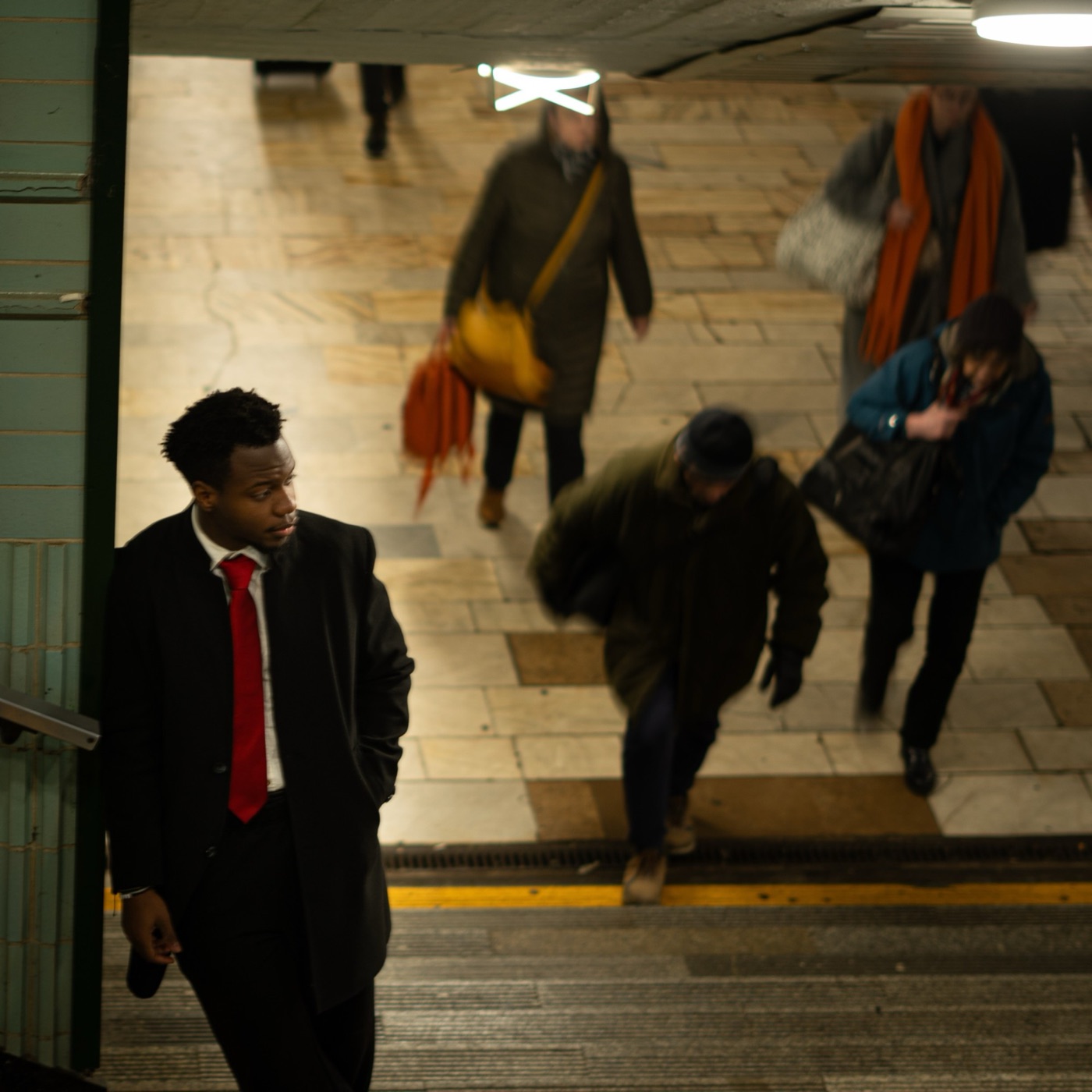 Kessy Janabi in a dark coat and red tie on the stairs of an underpass